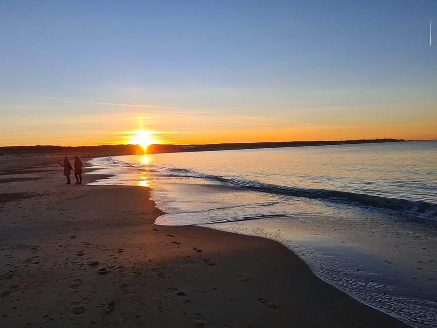 Zonsondergang boven zee, met twee wandelaars op het strand